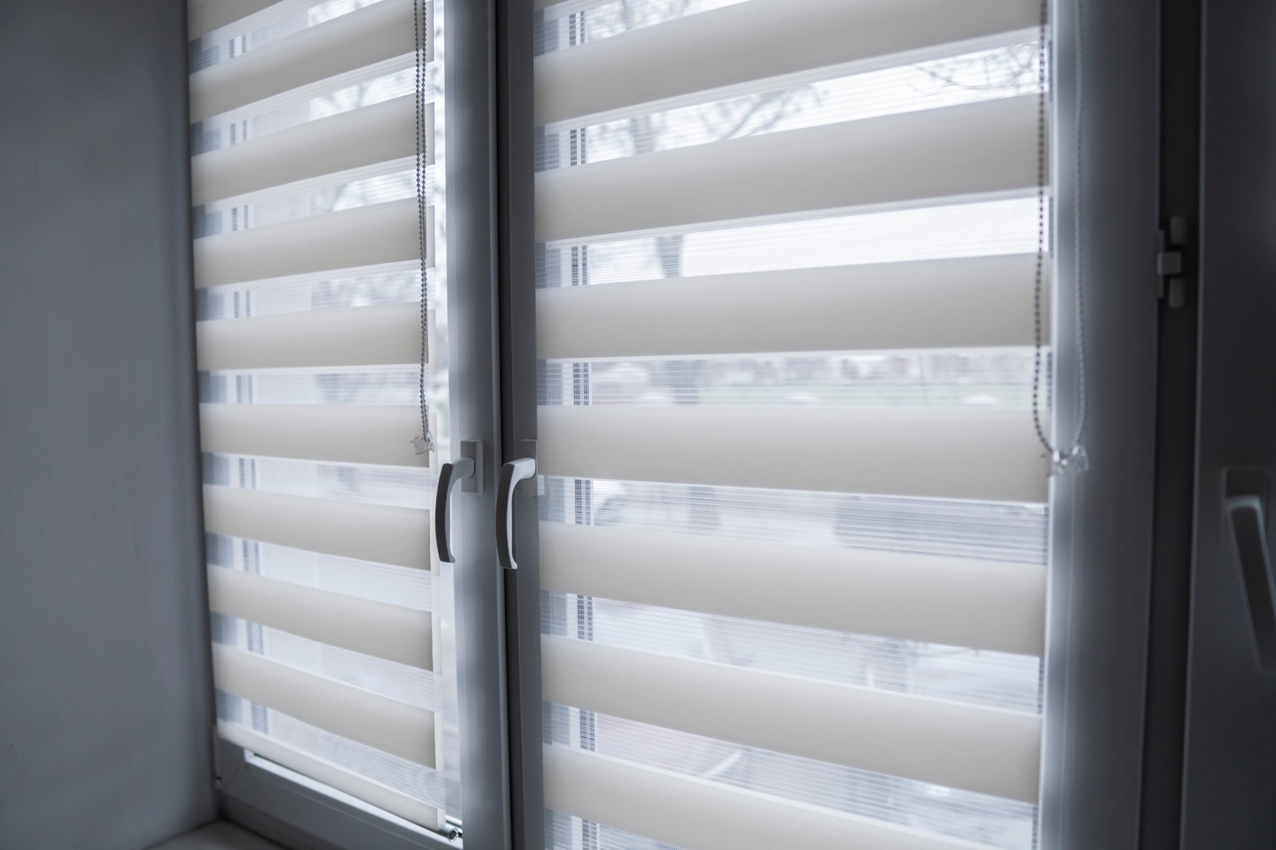 White fabric roller blinds on the white plastic window in the living room. Roll curtains indoor.